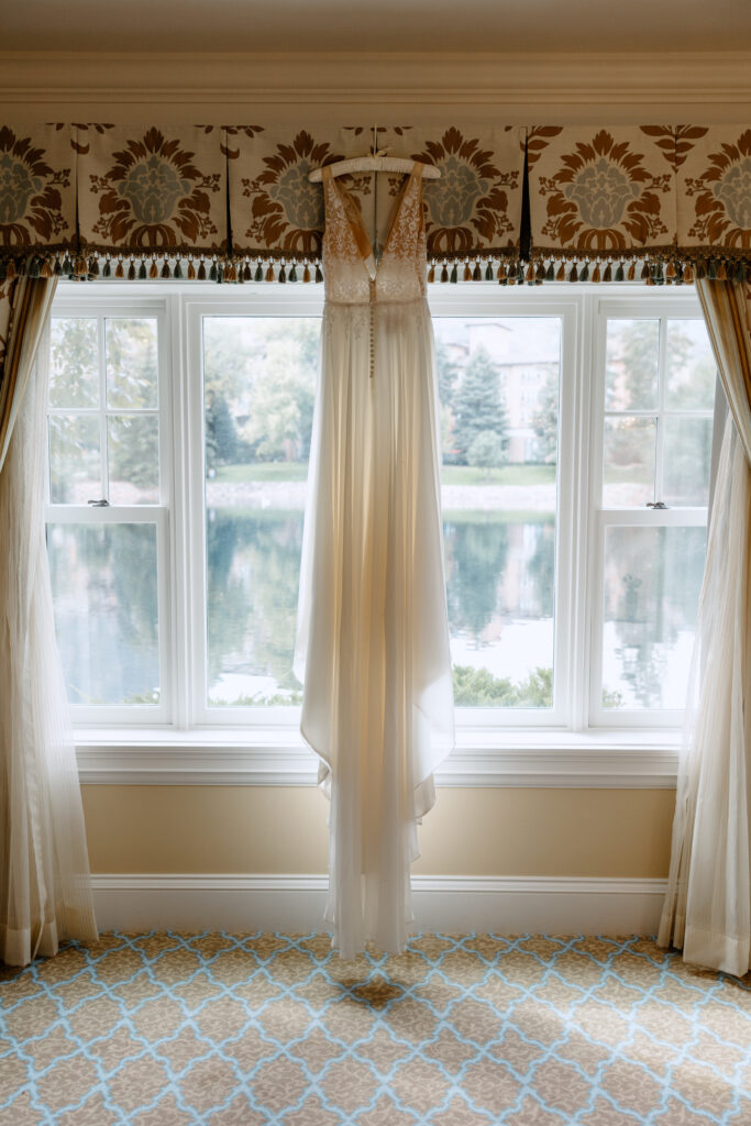 A bride's getting ready details with her dress hanging in the window