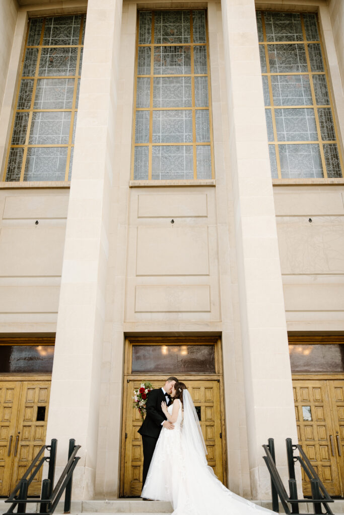 bride and groom kissing in front of architectural church