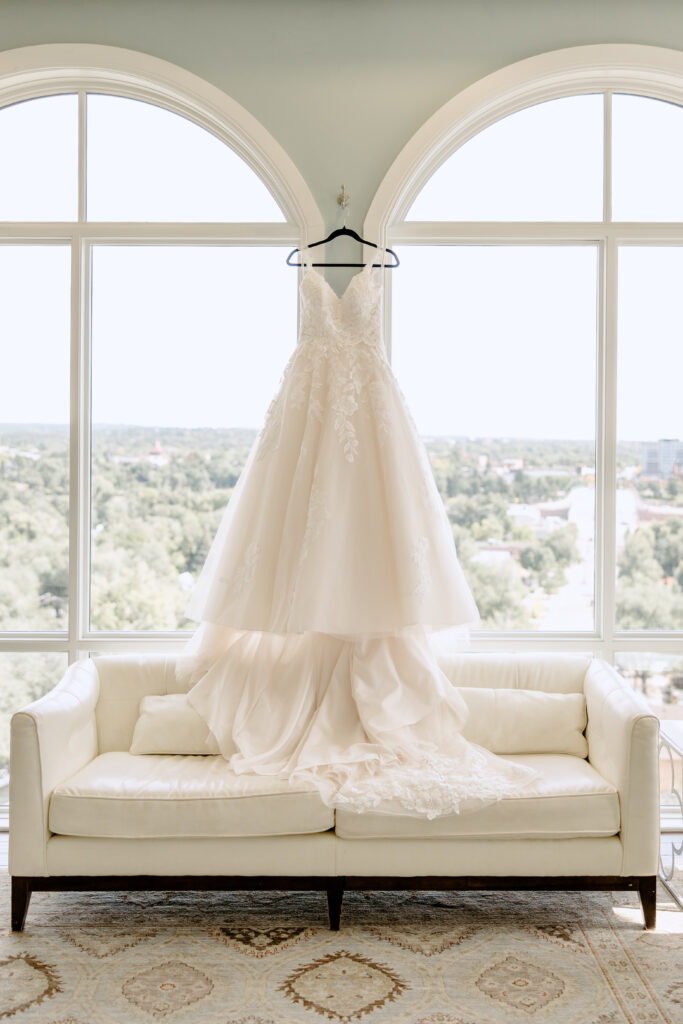 wedding dress hanging on window of getting ready room
