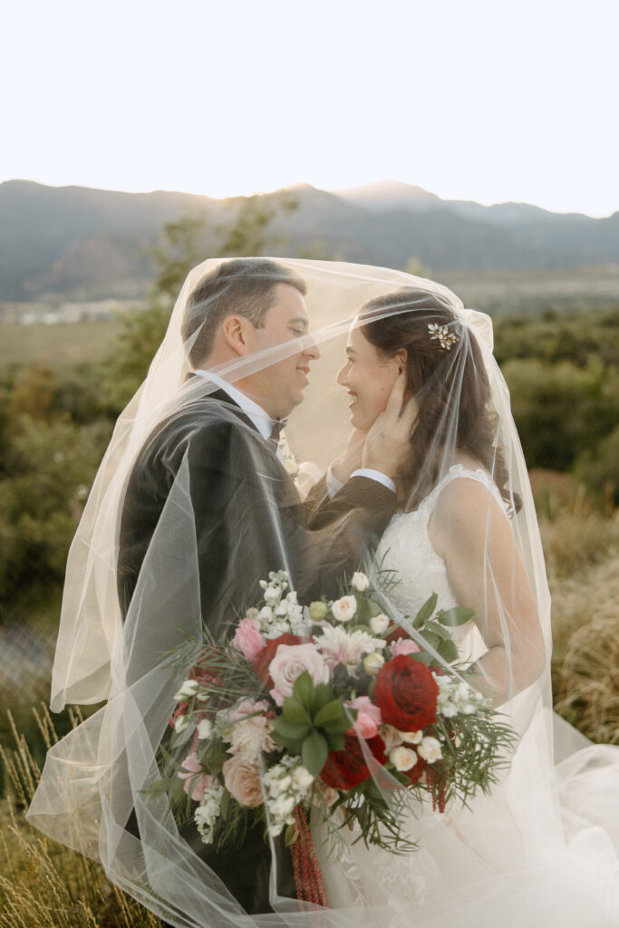 sunset photos of bride and groom under the veil with mountains behind them