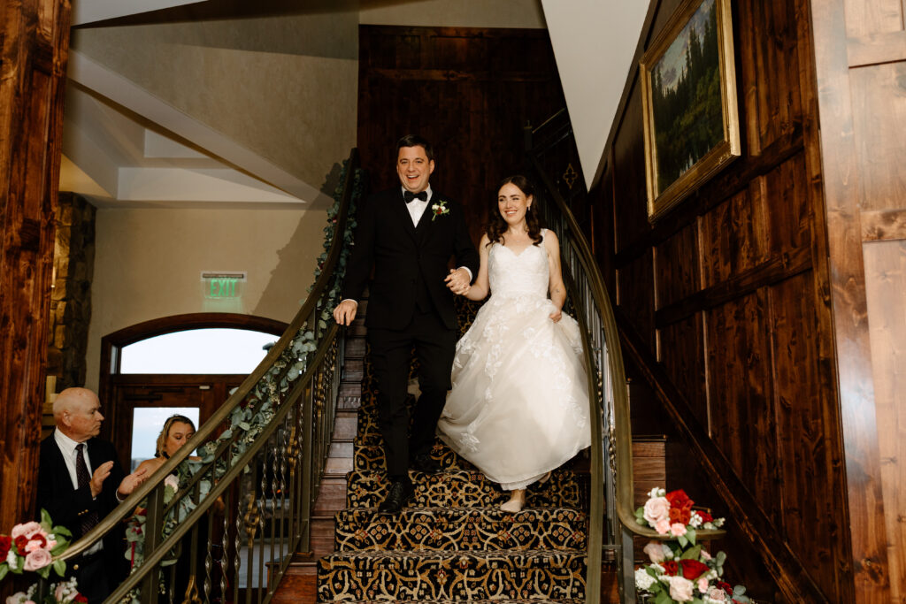 bride and groom coming down grand staircase at colorado springs wedding venue